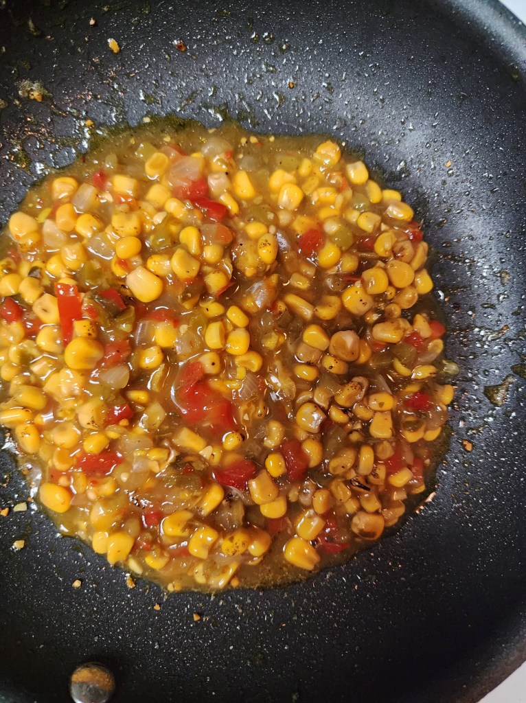 Sautéed corn mixed with diced tomatoes and bell peppers in a black frying pan.